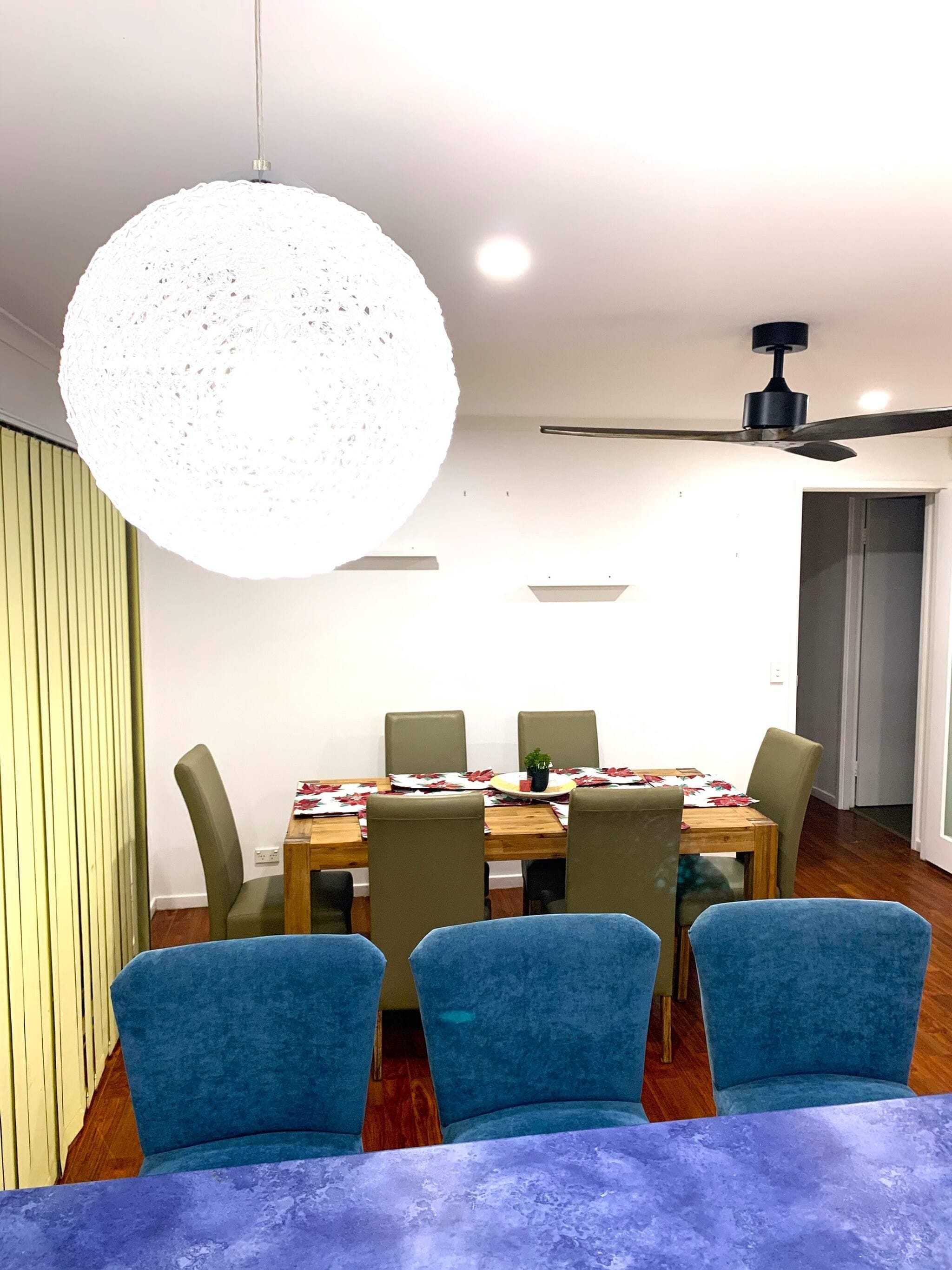 A dining area with a round table, six chairs, a ceiling fan, and a large pendant light.