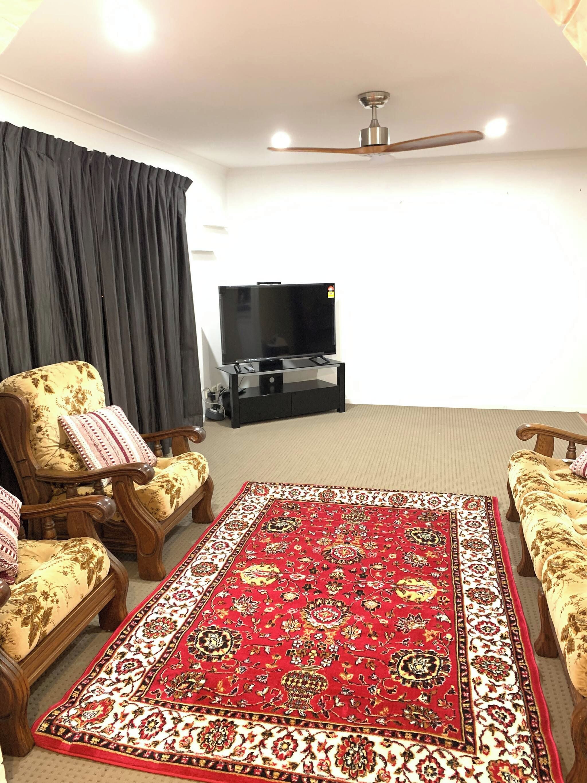 A living room with a flat-screen TV, a ceiling fan, and a patterned rug.