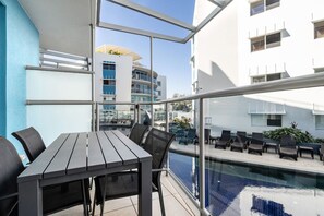 A balcony with a pool, outdoor seating, and a view of a modern building. - 2 Bedroom Pool Entry Apartment (Kings Beach)