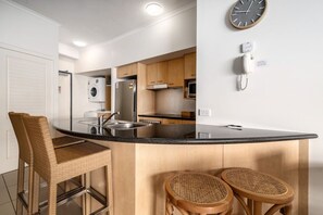 Una cocina moderna con una isla central, taburetes de bar, un reloj y un teléfono en la pared.