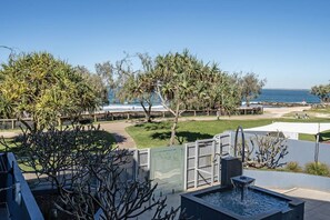 Eine Terrasse mit Wasserspiel, Blick auf den Ozean und einem von Bäumen gesäumten, eingezäunten Garten.