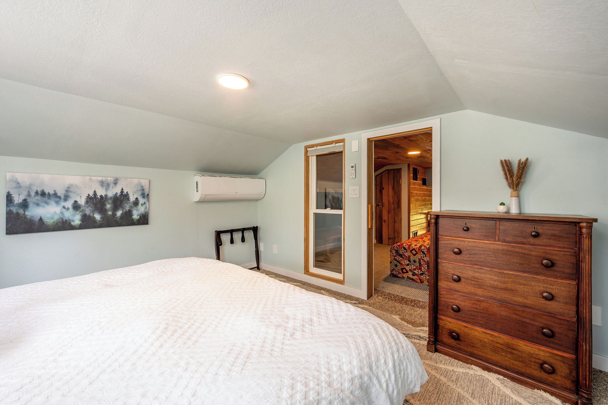 A bedroom with a bed, dresser, and a painting on the wall.