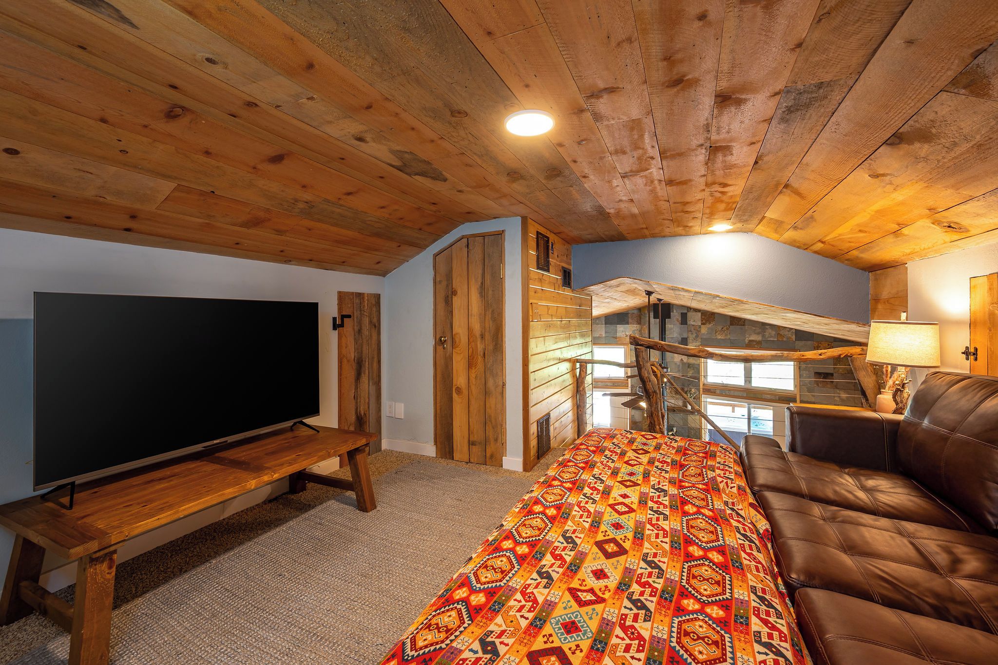 A cozy living room with a flat-screen TV, a sofa, a patterned rug, and a staircase leading to an upper level.