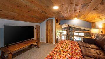 A cozy living room with a flat-screen TV, a sofa, a patterned rug, and a staircase leading to an upper level.