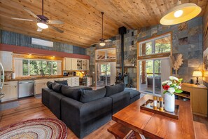 A modern interior with a wooden ceiling, a black sofa, a wooden dining table, and a kitchen area with a stone backsplash. - Waterfall Retreat at Peppermint Falls (Springville)