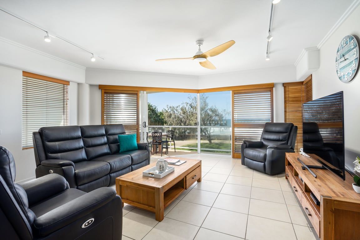 A modern living room with a black leather sofa, a wooden coffee table, a TV stand, and a ceiling fan.