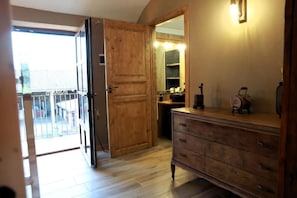 Una habitación con puerta de madera, cómoda, espejo y balcón con barandilla.