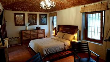 A bedroom with a large bed, wooden headboard, a nightstand, a dresser, and a window with a view.
