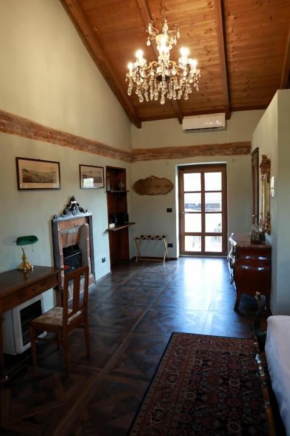 Una habitación amplia con techo de madera, un candelabro, chimenea, escritorio y un ventanal grande.