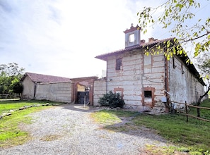 Un edificio rústico con fachada de ladrillo, una pequeña torre de campanas y un camino de grava que conduce a una entrada con portón.