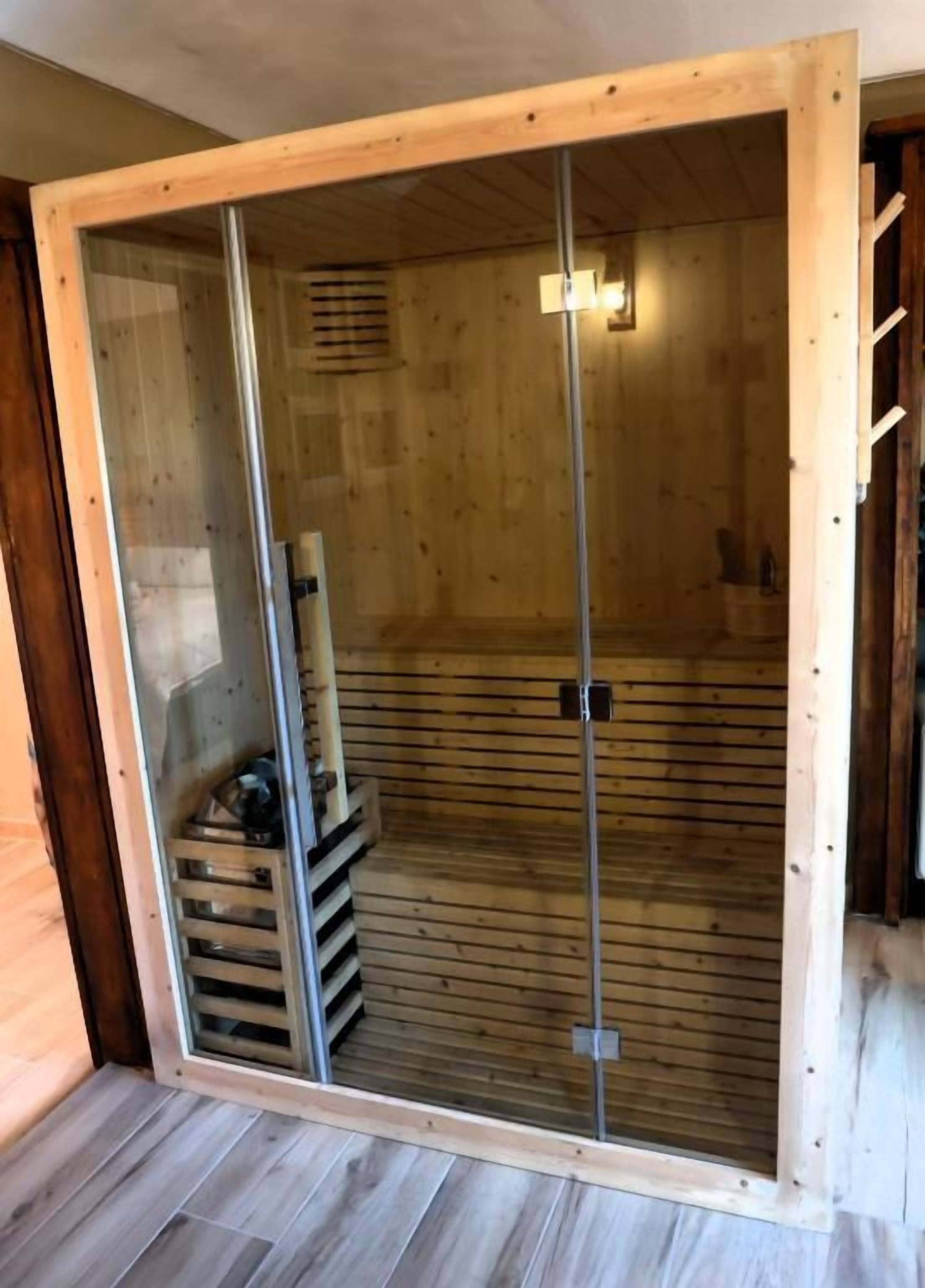 A sauna room with a wooden interior, a glass door, and a bench.