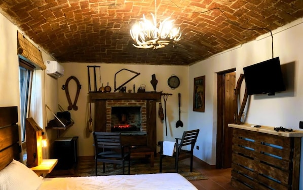 Una habitación con techo de ladrillo, chimenea, cama, escritorio y televisor montado en la pared.