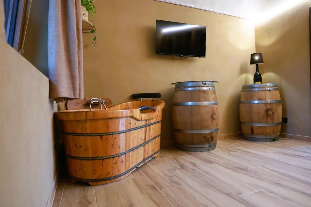 A room with wooden barrels, a television mounted on the wall, and a lamp on a barrel.