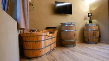 A room with wooden barrels, a television mounted on the wall, and a lamp on a barrel.