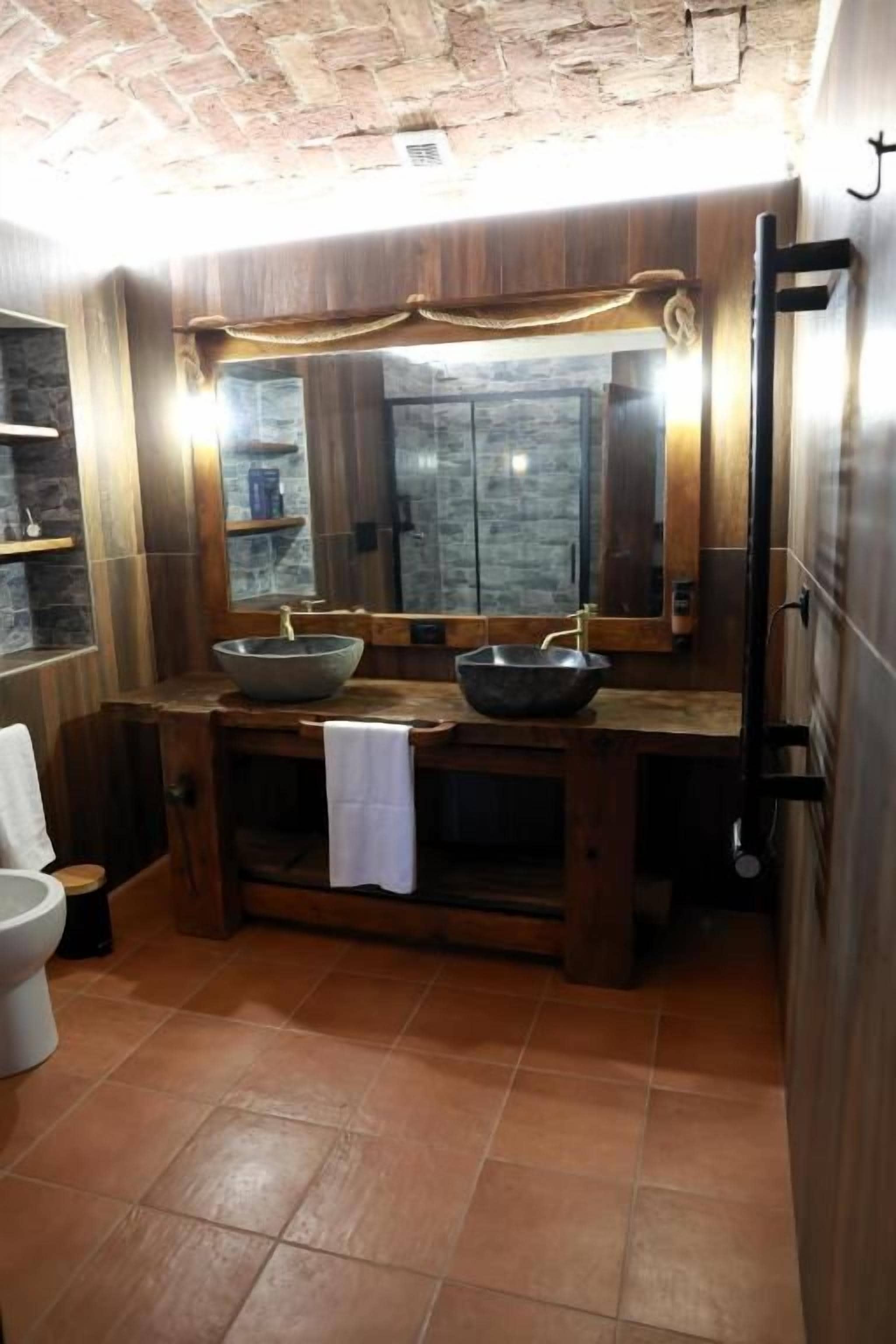 Une salle de bain avec un meuble-lavabo en bois, deux vasques, un grand miroir et une serviette accrochée au mur.