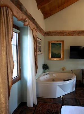 Un baño con una bañera, una ventana con cortinas, un cuadro en la pared y un televisor sobre la bañera.