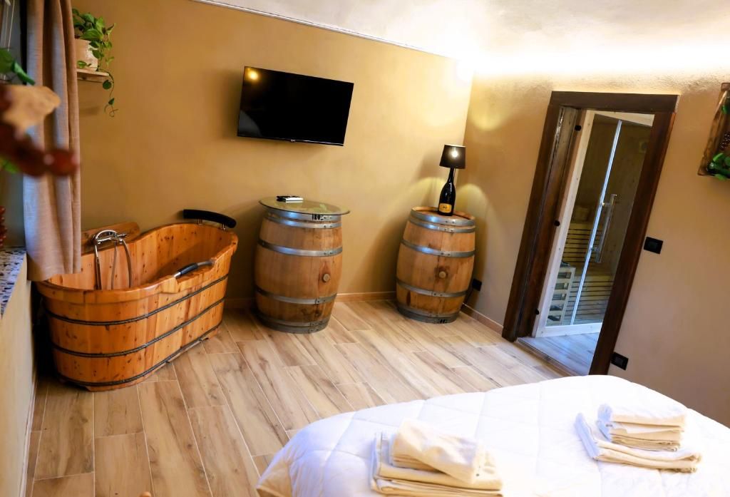 A room with a wooden bathtub, two wooden barrels, a flat-screen TV, and a bed with neatly folded towels.