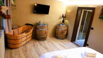 A room with a wooden bathtub, two wooden barrels, a flat-screen TV, and a bed with neatly folded towels.