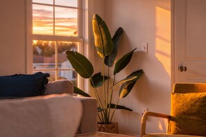 A room with a bed, a chair, and a large plant near a window with a view of the sunset. - Banana Villa - Tropical 4BR Pond-Front Home w/ Private Hot Tub (Walk to Beach) (North Myrtle Beach)