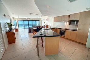 A modern kitchen with a central island, wooden cabinets, and a view to the outside. - 2 Bedroom Oceanfront Rooftop (Kings Beach)