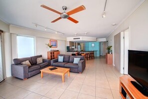 A spacious living room with a ceiling fan, a TV, and a kitchen in the background. - 2 Bedroom Oceanfront Rooftop (Kings Beach)