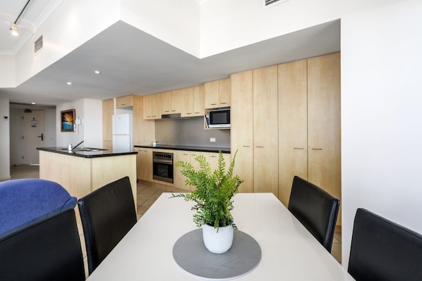 A modern kitchen with wooden cabinets, a central island, and a dining area with a table and chairs. - 2 Bedroom Poolside Rooftop No Balcony (Kings Beach)