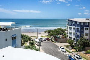 A beachfront hotel with a view of the ocean, parking area, and a building with a sign that reads 'Panda Nus'. - 2 Bedroom Poolside Rooftop No Balcony (Kings Beach)