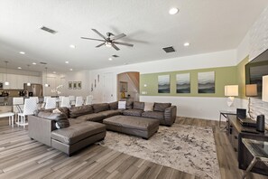 Ein modernes Wohnzimmer mit einem Ecksofa, einem Essbereich und einer Küche im Hintergrund.