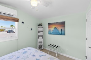 A bedroom with a bed, a window, a shelf with towels, a painting of a sunset, and a starfish decoration. - Upscale Oceanfront Retreat - 47' Seawall, Boats up to 44', Sleeps 6 & Pet Friendly! (Cudjoe Key)