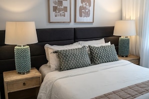 Ein ordentlich bezogenes Bett mit einer gesteppten Decke, zwei gemusterten Kissen und zwei Nachttischlampen auf Holznachttischen.