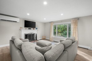 Un salon moderne doté d’une cheminée, d’un téléviseur à écran plat et d’une grande fenêtre avec des rideaux.