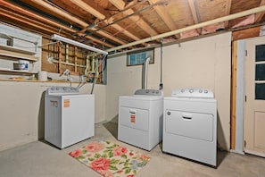 Ein Waschraum mit drei übereinander gestapelten Waschmaschinen und Trocknern, Holzbalken an der Decke, freiliegender Elektroinstallation und einem Blumenmuster-Teppich.