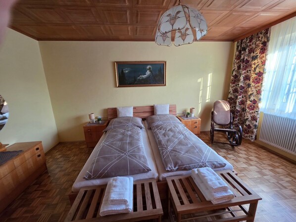 Un letto matrimoniale con una coperta a motivi geometrici, un comodino con una lampada, un quadro appeso al muro e una finestra con tende floreali.