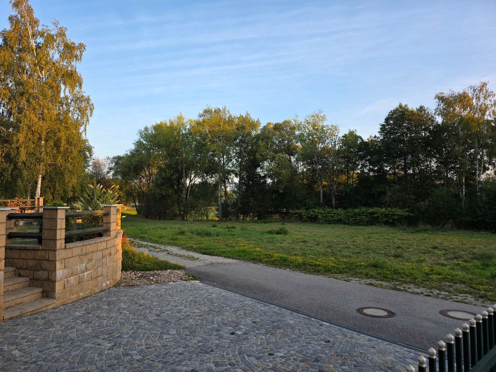 En asfalterad gångväg som leder genom en park, med en stenmur på ena sidan och träd i bakgrunden.