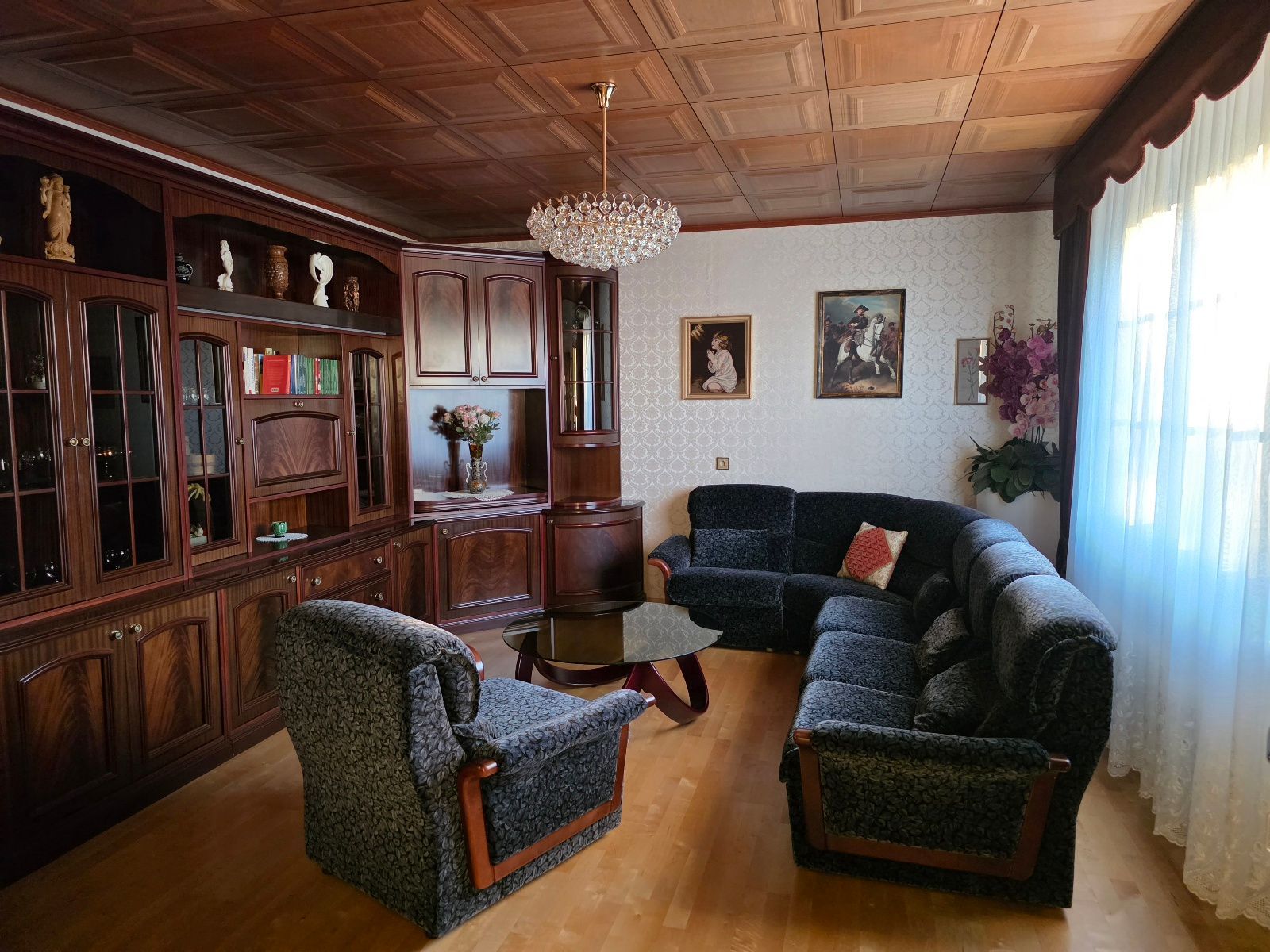 A traditional living room with wooden furniture, a chandelier, and artwork on the walls.