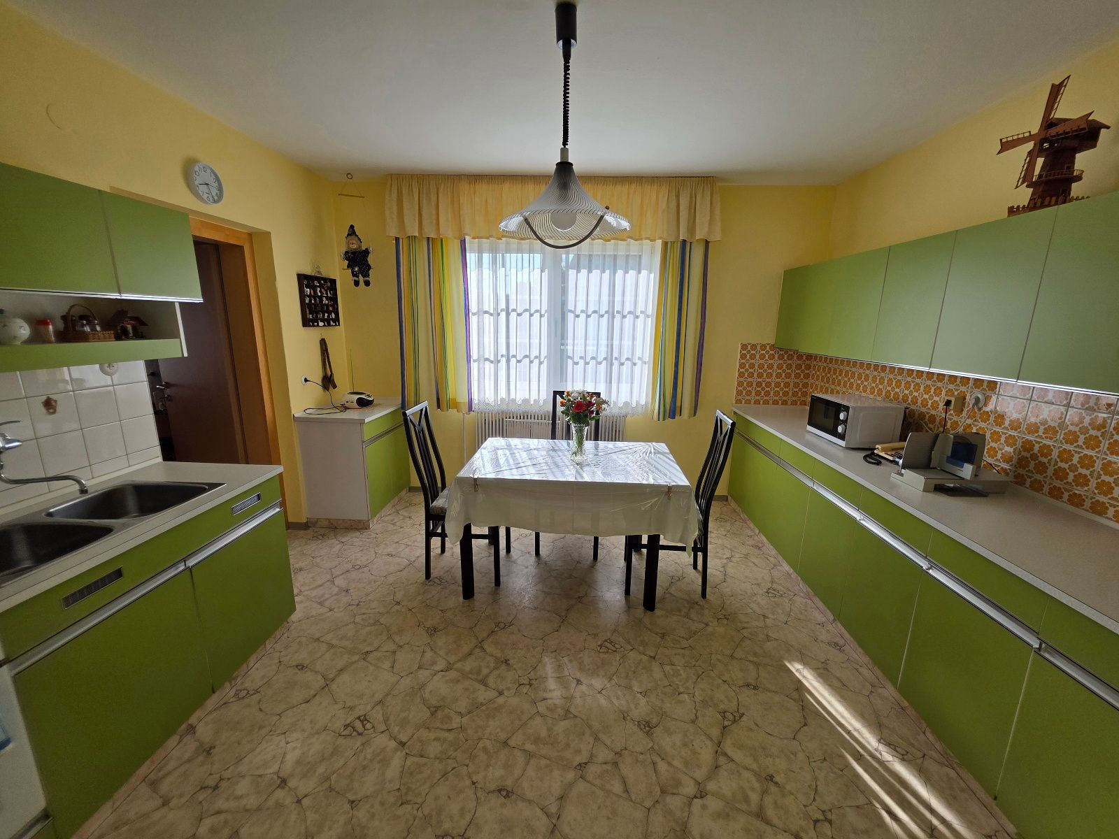 A kitchen with a dining table, chairs, a clock, and a windmill decoration.
