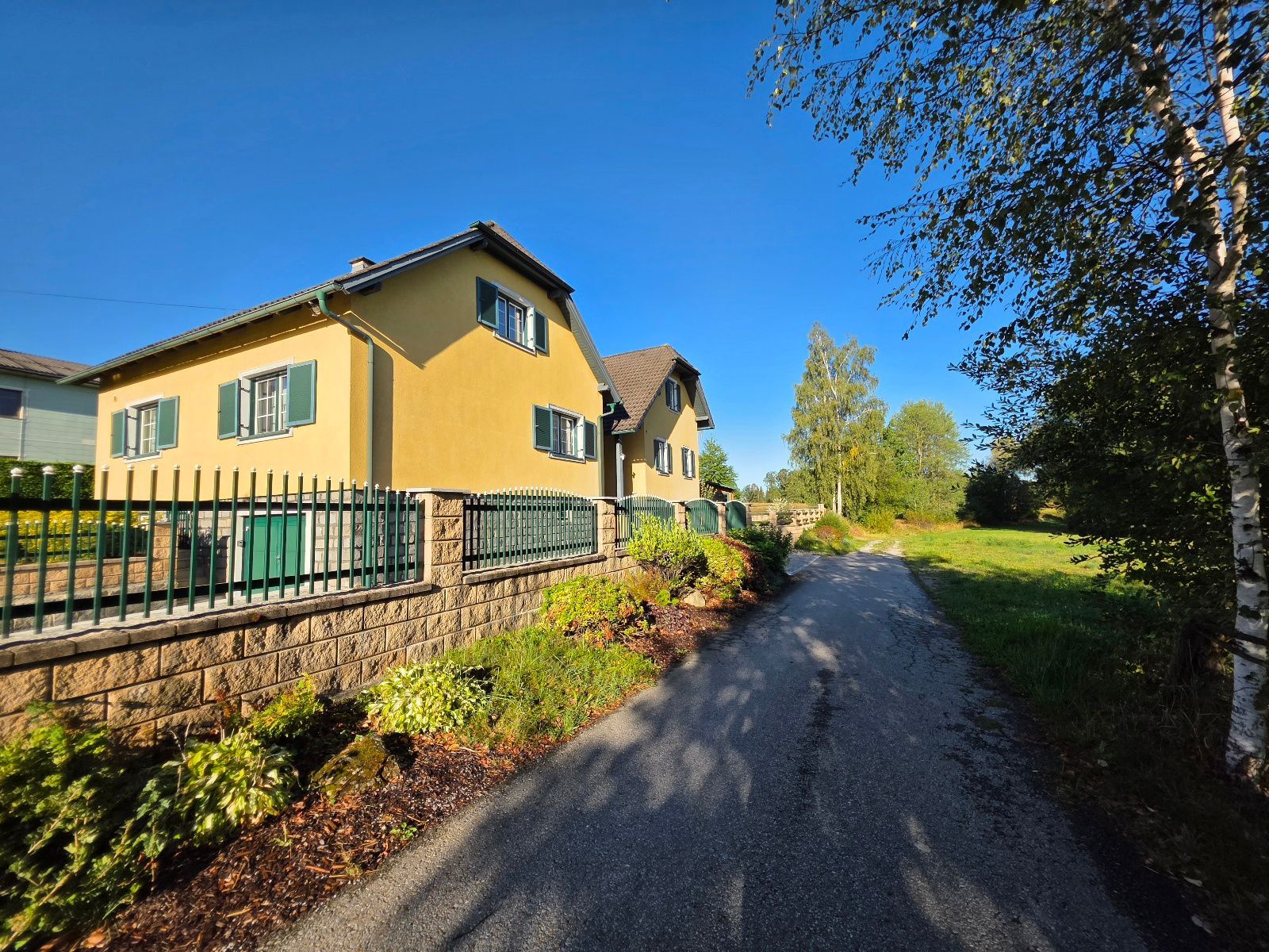A yellow house with a stone wall and a metal fence.