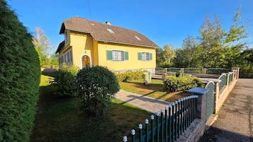 Een geel huis met een groene hek, een verharde oprit en een verzorgde tuin.