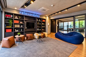 Un área de descanso moderna con un sillón orejero azul grande, un televisor de pantalla plana y un letrero de neón que dice 'relaxandplay'.