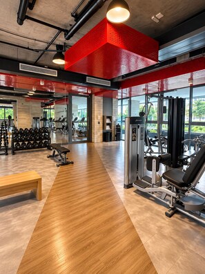 Un gimnasio con diversos equipos de ejercicio, un banco de madera y un rack de sentadillas fijado a la pared.