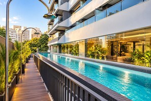 A modern building with a rooftop swimming pool, outdoor seating, and a view of the city. - Studio apartment in Pinheiros | Near Oscar Freire Metro Station, swimming pool and gym. (São Paulo)