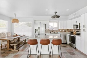 A modern kitchen with white cabinets, stainless steel appliances, and a central island with stools. - Private Pool | Game Room | Mesa Family Retreat (Mesa)