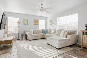 Ein modernes Wohnzimmer mit Ecksofa, Couchtisch, Stehlampe und Deckenventilator.