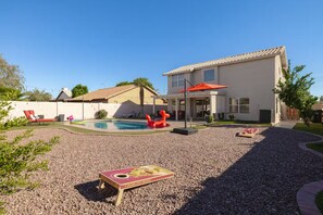 Ein Wohnhausgarten mit Swimmingpool, Gartenmöbeln und einer überdachten Terrasse.