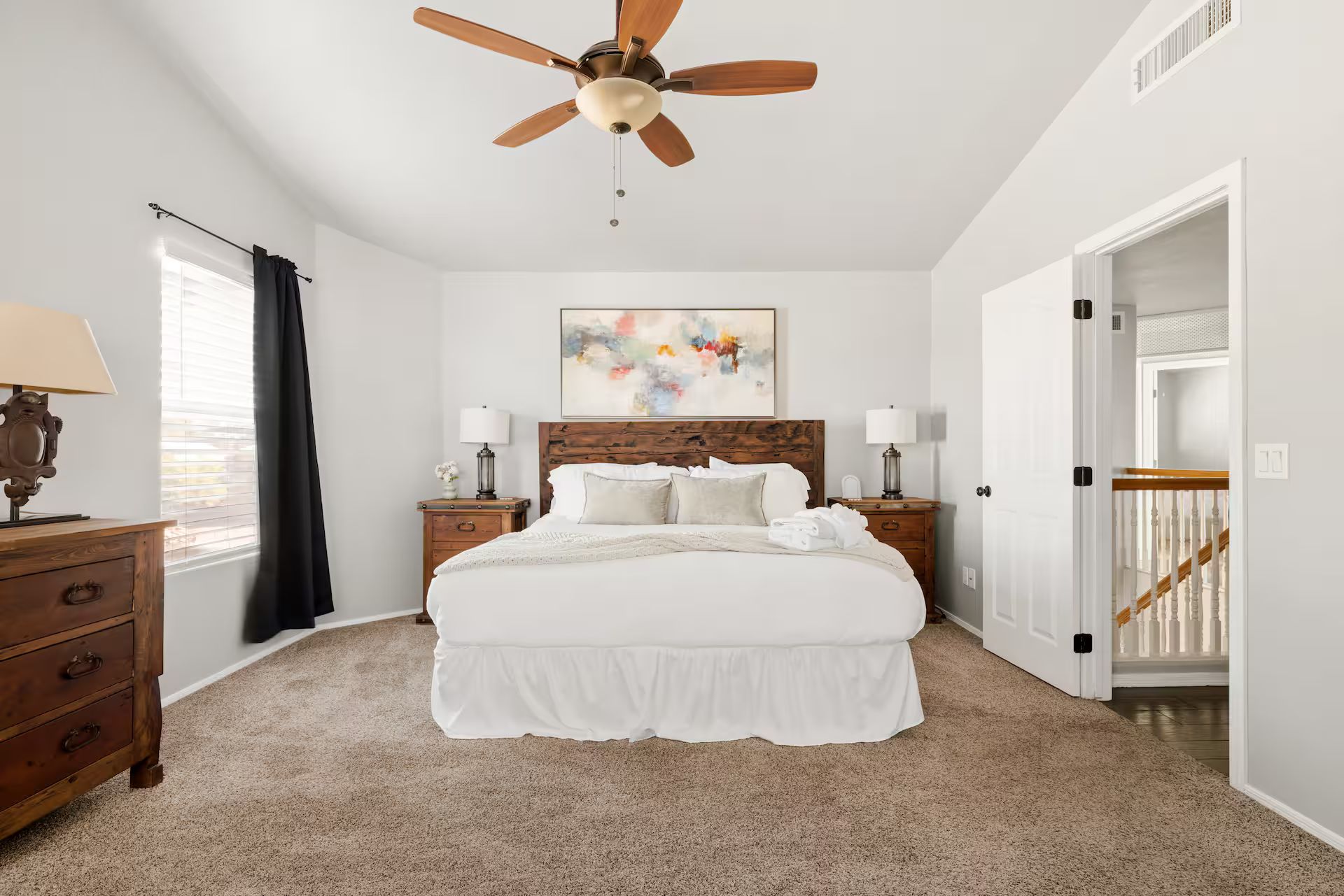 A bedroom with a bed, nightstands, a ceiling fan, a window with curtains, and a painting on the wall.