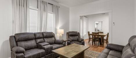 A living room with a sofa, armchair, and coffee table. There is a dining area with a table and chairs.