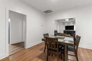 Ein Essbereich mit Holztisch und -stühlen, einem Fernseher im Hintergrund und einem Deckenlüfter.