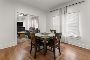 Un área de comedor con una mesa y sillas de madera, un sofá y un televisor al fondo.