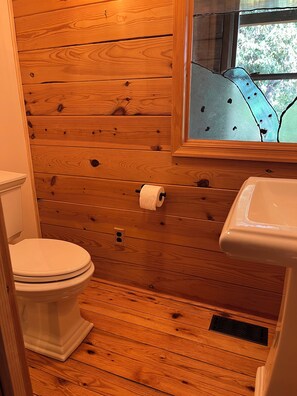 Ein Badezimmer mit Holzwänden, einer Toilette, einem Waschbecken und einem Fenster.