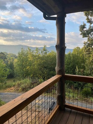 Eine Holzterrasse mit Metallgeländer, die auf einen bewaldeten Bereich und ferne Hügel blickt.
